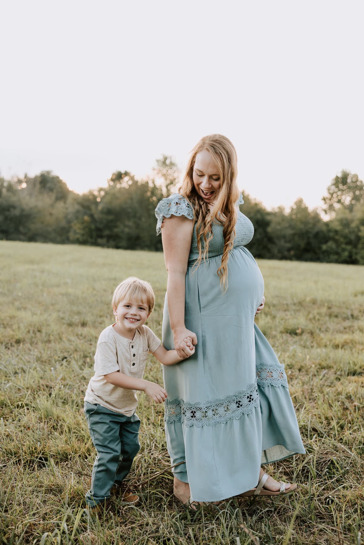 An expecting mother holding hands with her young son in a field